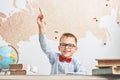 A happy, joyful schoolboy wears glasses, sits at a desk and raised his hand upwards Royalty Free Stock Photo