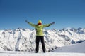 Happy joyful woman in ski suit having fun outdoors in winter, standing on the mountains covered with snow with raised up Royalty Free Stock Photo
