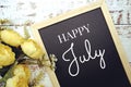 Happy July text on background decorated with flower bouquet on wooden background