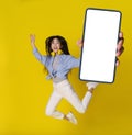 Happy jumping asian girl with smartphone in hand showing white screen mobile app advertisement isolated on yellow Royalty Free Stock Photo