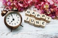 Happy June with alarm clock on wooden background