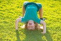 Happy kid boy girl standing upside down on her head on grass in summer day. Royalty Free Stock Photo