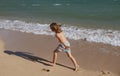 Happy kid boy have fun on tropical sea beach. Funny child run with splashes by water pool along surf edge. Kids activity Royalty Free Stock Photo