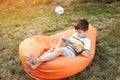 Happy kid boy playing game on smartphone in the park outdoor, child using smartphone on soft orange chair at home garden Royalty Free Stock Photo