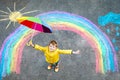 Happy kid boy in rubber boots with rainbow sun and clouds with rain drops painted with colorful chalks on ground or Royalty Free Stock Photo