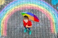 Happy kid boy in rubber boots with rainbow sun and clouds with rain drops painted with colorful chalks on ground or Royalty Free Stock Photo