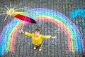 Happy kid boy in rubber boots with rainbow sun and clouds with rain drops painted with colorful chalks on ground or Royalty Free Stock Photo