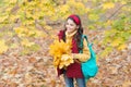 Happy kid in casual style spend time gathering fallen maple leaves in autumn park enjoying good weather carry backpack