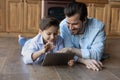 Happy kid and dad resting on heating floor, using tablet Royalty Free Stock Photo