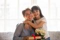 Happy kid daughter embracing mom holding flowers bouquet and gift