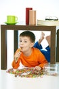 Happy kid eating lollipop under table sweets spilt Royalty Free Stock Photo