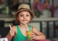 Happy kid girl drinking apple juice in restaurant and showing th Royalty Free Stock Photo