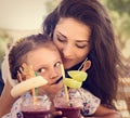 Happy kid girl and funny emotional mother drinking berries smoothie juice together in street summer outdoor cafe. Closeup