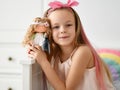 Happy kid girl in home clothing and headband with bow plays takes picture is posing with her favorite doll at home Royalty Free Stock Photo