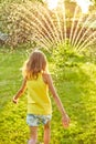 Happy kid girl playing with garden sprinkler run and jump, summer Royalty Free Stock Photo