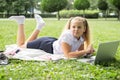 happy kid girl on school uniform with notebook has online lesson on laptop on lawn