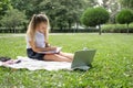 happy kid girl on school uniform with notebook has online lesson on laptop on lawn