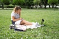 happy kid girl on school uniform with notebook has online lesson on laptop on lawn