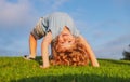 Happy kid girl standing upside down on her head on grass in summer day. Royalty Free Stock Photo