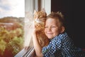 Happy kid hug ginger cat while stay at home. Cat and boy looking out of the window. Self quarantine concept. Big pet cat Royalty Free Stock Photo