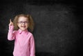 Happy kid inventor with rised hand thinking and finding idea near school black chalkboard