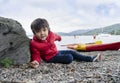 Happy kid lying on pebbles with blurry people kayaking background, Chid layingdown and pointing out to the lake, little boy