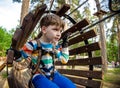 Happy kid overcomes obstacles in rope adventure park. Summer holidays concept. Little boy playing at rope adventure park. Modern Royalty Free Stock Photo