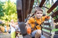 Happy kid overcomes obstacles in rope adventure park. Summer holidays concept. Little boy playing at rope adventure park. Modern Royalty Free Stock Photo