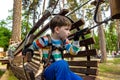 Happy kid overcomes obstacles in rope adventure park. Summer holidays concept. Little boy playing at rope adventure park. Modern Royalty Free Stock Photo