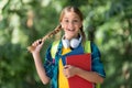 Happy kid with pigtails carry school books for foreign language learning wearing headphones natural landscape, English Royalty Free Stock Photo