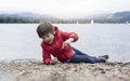 Happy kid playing pebbles and leaves with blurry nature background, Chid lyingdown on pebbles by the lake playing alone in sunny