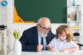 Happy kid in school. Old senior teacher help to writing. Education, teachering, elementary school. Private lesson. Royalty Free Stock Photo