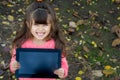 Happy kid showing tablet as if advertising it, and standing over autumn background