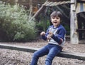 Happy kid sitting on his own playing with wooden stick in forest park, Active child wearing jumper playing outdoor in playground, Royalty Free Stock Photo