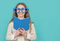 Happy kid smiling in big funny heart-shaped glasses holding open school book blue background Royalty Free Stock Photo