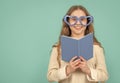 Happy kid smiling in big funny heart-shaped glasses holding open school book blue background Royalty Free Stock Photo