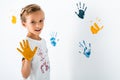 happy kid with yellow paint on hand near hand prints on white. Royalty Free Stock Photo