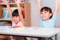 Happy kids with arms up sit in classroom. Cute girl taking lessons for home schooling Elementary school children enjoy learning Royalty Free Stock Photo