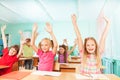Happy kids with arms up sit in classroom rows