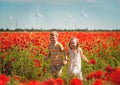 Happy kids boy and girl are running in red poppies field. School children playing with wind generators turbines Royalty Free Stock Photo