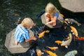 Kids walk by stepping stones, feeding koi fishes in pond Royalty Free Stock Photo