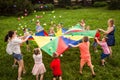 Happy kids waving rainbow parachute full of balls Royalty Free Stock Photo