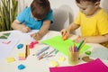 Happy kids with yellow and blue shirts doing arts and crafts together at their desk. Children draw on colored paper Royalty Free Stock Photo