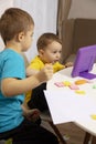 Happy kids with yellow and blue shirts doing arts and crafts together at their desk and watching cartoon on digital Royalty Free Stock Photo