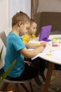 Happy kids with yellow and blue shirts doing arts and crafts together at their desk and watching cartoon on digital Royalty Free Stock Photo