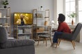 Happy woman sitting in chair in living-room and watching music video on television