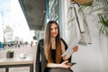 Happy lady in formal clothes sitting indoors with a document in her hand and looking into the camera with a smile on her face.