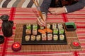 Happy lady holds a sushi roll on the chopsticks, looks at delicious Japanese food and smiles, over a table sit on a sofa Royalty Free Stock Photo