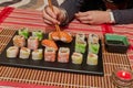 Happy lady holds a sushi roll on the chopsticks, looks at delicious Japanese food and smiles, over a table sit on a sofa Royalty Free Stock Photo