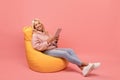 Happy lady using digital tablet while sitting in beanbag chair over pink background with free space Royalty Free Stock Photo